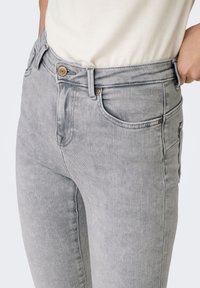 Ανοιχτό γκρι τζιν παντελόνι με εφαρμοστή γραμμή, πέντε τσέπες και διακριτικές ραφές. Διαθέτει μπροστινό κούμπωμα με κουμπί και φερμουάρ.