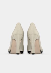 Μπεζ γόβες με λείο υφή, που διαθέτουν μαύρη λεπτομέρεια στη μύτη. Το σχήμα είναι κομψό με μυτερή μύτη και λεπτό τακούνι.