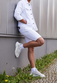 Chaqueta de mezclilla blanca y pantalones cortos combinados con zapatillas gris claro. El conjunto presenta líneas limpias y un corte relajado sobre un fondo texturizado.