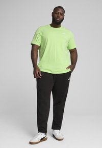Tricou scurt cu mânecă, de culoare verde deschis, cu logo, asortat cu pantaloni de trening negri și adidași albi. Textură netedă, croială lejeră și design minimal.