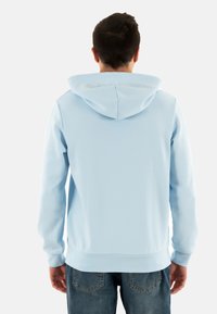 Sudadera con capucha azul claro, de manga larga, con puños elásticos y un bolsillo canguro en la parte delantera. Tejido suave con una textura lisa.