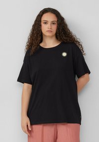 Schwarzes Baumwoll-T-Shirt mit rundem Hals, kurzen Ärmeln und einem goldenen Sonnen-Icon auf der linken Brust. Lockere Passform und weicher Stoff.