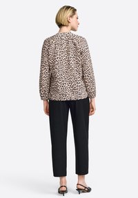 Beige Bluse mit Leopardenmuster, langen Ärmeln und Rundhalsausschnitt, kombiniert mit lockeren schwarzen Hosen und schlichten schwarzen Sandalen.
