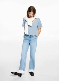 Ljusblå bomullströja, lös passform, v-ringning. Ljusblå denimjeans med fransad vit fåll, i kombination med mörka loafers. Vit stickad scarf draperad.