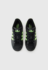 Baskets Adidas noires avec des rayures vert fluo, lacets noués, vues de dessus sur un fond blanc uni.