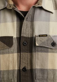 Koszula z guzikami w wzór houndstooth, w odcieniach beżu i brązu, z kieszeniami na piersi oraz metką PME Legend przy lewej kieszeni.