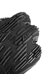 Schwarzer Sportschuh mit einer strukturierten Gummisohle mit Rillen, Mesh-Obermaterial und sichtbarem Branding an der Seite. Nahaufnahme.
