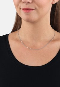 Collana in argento con un design elegante e liscio. Presenta una texture sottile e scintillante ed è indossata su un capo nero.