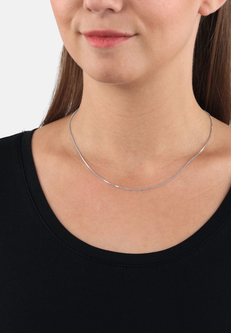 Collana in argento con un design elegante e liscio. Presenta una texture sottile e scintillante ed è indossata su un capo nero.