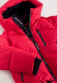 Rote Daunenjacke mit Kapuze, ausgestattet mit schwarzen Reißverschlüssen und Akzenten. Großes Steppdesign und markiertes Innenetikett. Warmes, gestepptes Material.