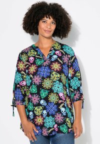 Schwarze Bluse mit bunten Blumen- und Totenkopf-Mustern, Dreiviertelärmel und V-Ausschnitt. Der Stoff wirkt glatt mit einem leicht schimmernden Finish.