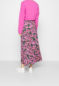 Falda larga con estampado floral en verde con flores rosas, combinada con un suéter rosa brillante y zapatillas blancas. Presenta un diseño fluido y una textura suave.