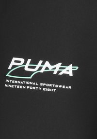 Vêtements de sport noirs avec "PUMA" en lettres blanches en gras, et "INTERNATIONAL SPORTSWEAR" ainsi que "NINETEEN FORTY EIGHT" en plus petite police en dessous.