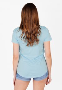Camiseta de manga corta azul claro con cuello redondo, hecha de algodón suave. Presenta un dobladillo ligeramente curvado en la parte trasera y una textura suave.
