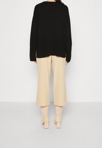 Svart stickad tröja med avslappnad passform, som har vida ärmar och en texturerad ribbad nederkant. Parat med beige vida byxor och stövlar med klack.