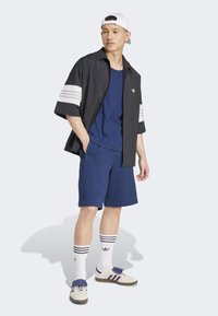 Μαύρο κοντομάνικο μπουφάν με φερμουάρ και λευκές ρίγες, μπλε αμάνικος τοπ, ναυτικές σορτς, λευκές κάλτσες με ναυτικές ρίγες και λευκά παπούτσια με πολύχρωμες λεπτομέρειες.