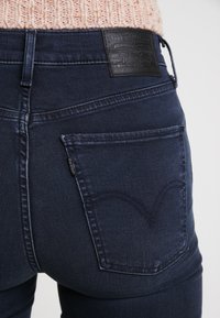 Jeans de denim oscuro con un diseño clásico. Bolsillo trasero con un patrón de arco cosido y una etiqueta de cuero con el logo de la marca.