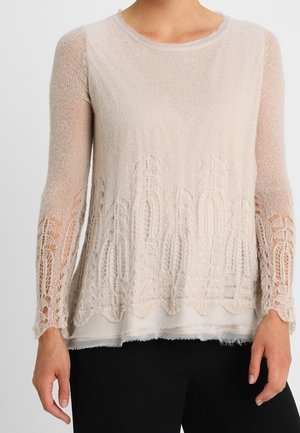 Maglione lavorato a maglia di un beige chiaro con maniche lunghe, caratterizzato da un motivo in pizzo all'orlo e nelle maniche, sovrapposto a una base bianca.