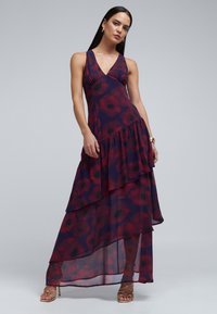 Maxi šaty z průhledné tmavě fialové látky s květinovým vzorem v červené a černé barvě. Mají výstřih do V, vrstevnatý design a rozšířený lem.