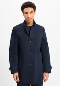 Navyjas gemaakt van een gladde stof, met een hoge kraag, sluiting met drie knopen, zijzakken en verstelbare manchetten.