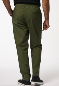 Olivgrüne Hose mit lockerem Schnitt, elastischem Bund und zwei Gesäßtaschen. Kombiniert mit schwarzen High-Top-Sneakern.