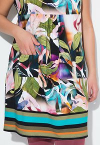 Šaty s květinovým potiskem zdobené živými listy v zelené, růžové a modré barvě. Obsahují dvě přední kapsy a pruhovaný lem v několika barvách.
