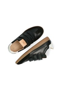 Baskets en cuir noir avec trois bandes Velcro, une semelle en caoutchouc et un accent de talon blanc. Présente des surfaces lisses et texturées.