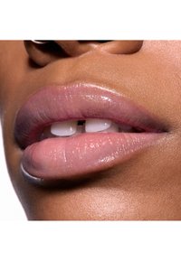 Nahaufnahme von glänzenden, hellrosa Lippen mit einer natürlichen Form, die eine leichte Textur aufweisen und zwischen ihnen sichtbare Zähne zeigen. Der Hintergrund ist neutral.