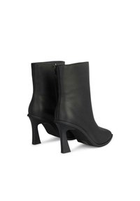 Botas de tobillo de cuero negro con punta redondeada, un alto tacón de aguja y cremallera trasera. Textura suave con un diseño minimalista.