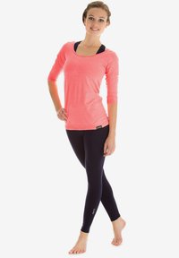 Lichte koraalkleurige langevleugel top met ruime halslijn, gecombineerd met aansluitende zwarte leggings. Soepele textuur; ontworpen voor actieve kleding.