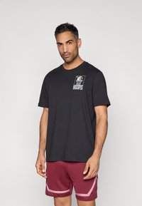 Zwart katoenen T-shirt met korte mouwen, met een witte grafische print van een basketbal en het "HOOPS"-logo op de borst.