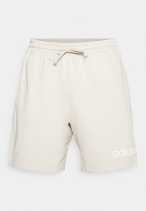 Beige shorts lavet af blødt bomuldsblanding, med elastisk talje og snørre samt hvid Adidas logo på nederste venstre side.