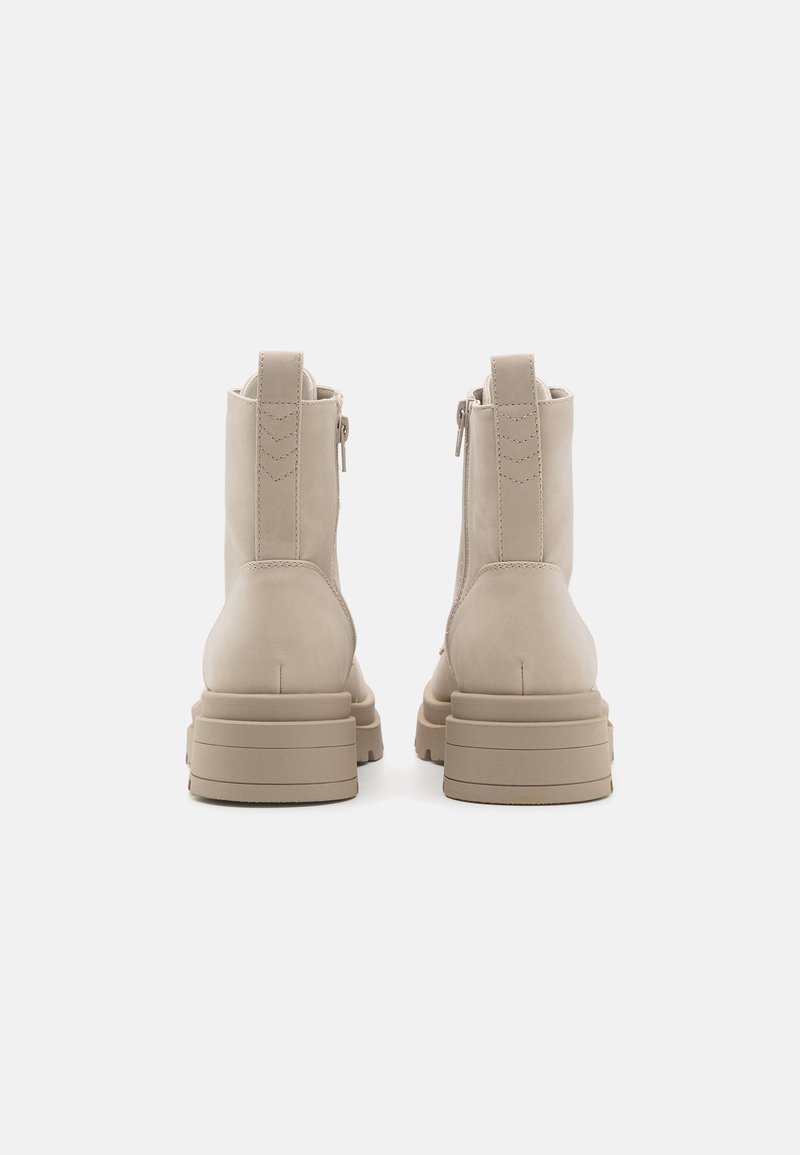 Bottines beige avec une finition en daim lisse, des fermetures éclair sur les côtés et une semelle épaisse et crantée. Présente des coutures minimalistes et une languette.