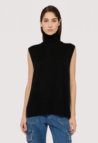 Černý pletený bezrukávový rolák s ribbovanou strukturou, s volným střihem a bočními rozparky. Nosený s modrými džínovými cargo kalhotami.