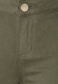Olijfgroene denimpantalon met een voorzak, gouden knoop en een opvallend stikselpatroon langs de tailleband en zijnaden.