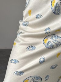 Hvit stoff med et mønster av østers og sitroner, med varierende nyanser av blått for østersene og gult for sitronskivene. Glatt tekstur.