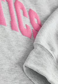 Hall grey sweatshirts, mille roosa tekstuuriga tähed, pehme kangapind ja varruka detail. Kujundus rõhutab mugavust ja vabaaega.