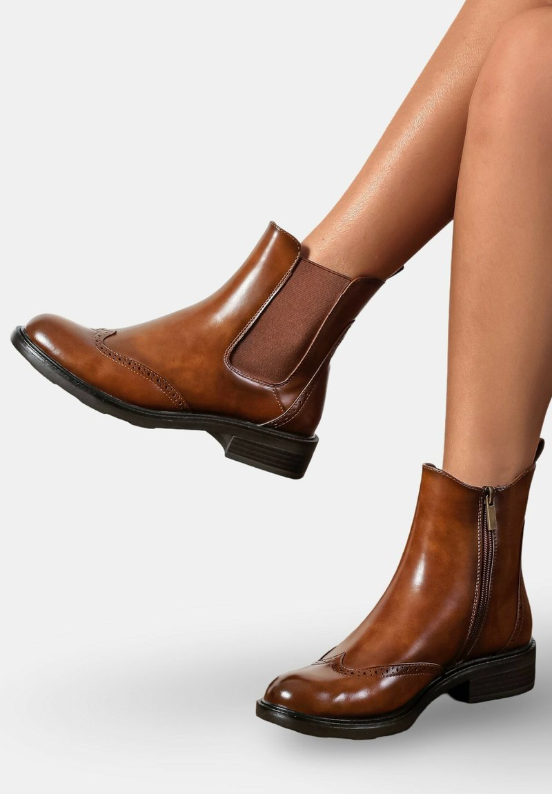 Bottes en cuir marron jusqu'à la cheville avec des panneaux élastiques latéraux, des perforations décoratives et un petit talon bloc. Fermeture éclair sur le côté pour un enfilage facile.