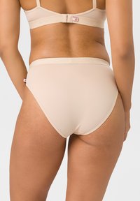 Beige nahtlose Unterwäsche mit glatter Textur, hoher Bundhöhe und elastischem Taillenbund. Verfügt über ein kleines Logo-Etikett an der Seite.