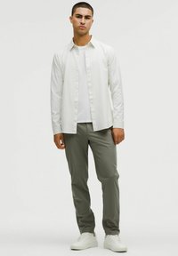 Biała koszula o kroju slim z białym T-shirtem, w zestawieniu z jasnoszarymi spodniami i białymi sneakersami. Gładki materiał i dopasowany fason.