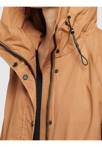 Giacca marrone resistente all'acqua con cappuccio, cordoncino regolabile, zip frontale e bottoni a pressione. Texture liscia con dettagli neri a contrasto.