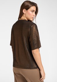 Kortærmet top i metallisk bronze med en glat, skinnende tekstur og en afslappet pasform. Bagsiden har en rund halsudskæring og en diskret glans.