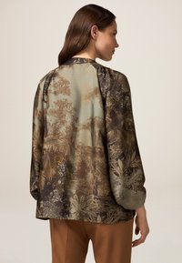 Bluzka z szyfonu w tropikalny wzór liści w ziemistych odcieniach, z długimi rękawami, okrągłym dekoltem i luźnym krojem.