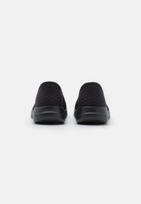 Czarne buty wsuwane z teksturowaną cholewką w diamentowy wzór oraz gładką, zaokrągloną podeszwą z gumy. Widok z tyłu ukazuje minimalistyczny design.