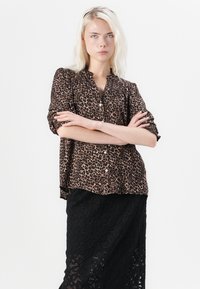 Hedvábná blůza s leopardím vzorem, s knoflíkovým zapínáním vpředu, dlouhými rukávy s ohrnutím k loktům a volným střihem, v kombinaci s černou krajkovou sukní.