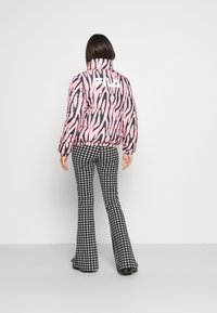 Giacca a vento a righe zebrate rosa e nera con colletto alto, dotata di un logo bianco. Abbinata a pantaloni a zampa d'elefante bianco e nero a motivo pied-de-poule.