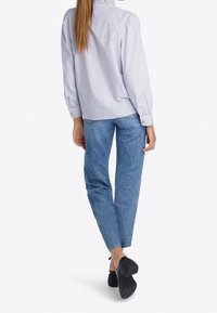 Blau-weiß gestreifte Bluse mit einem rüschierten Ausschnitt, kombiniert mit hellblauen Jeans und schwarzen High Heels. Mit knöpfbaren Manschetten.