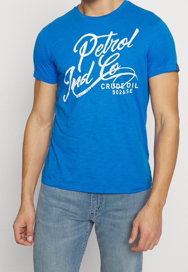 Blaues T-Shirt mit kurzen Ärmeln aus weichem Stoff, mit weißem Aufdruck "Petrol Ind Co" und "Crude Oil 5026.SE" auf der Vorderseite.