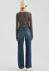Langärmliges Oberteil mit floralem Muster in dunklen Farben, kombiniert mit hochgeschnittenen, weit geschnittenen blauen Jeans mit fransigem Saum und zwei hinteren Taschen.