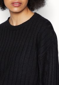 Czarny sweter z prążkowanej dzianiny z okrągłym dekoltem. Tekstura jest miękka, z pionowymi liniami i luźnym krojem.